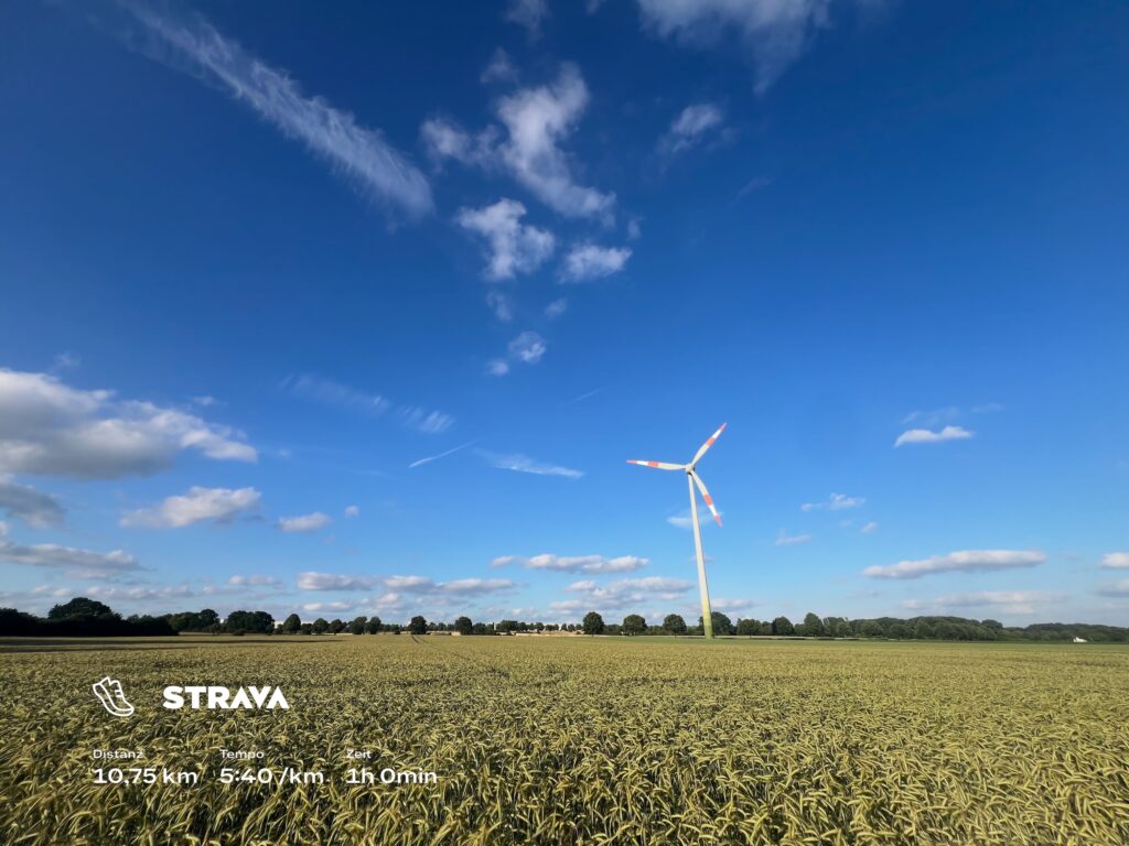 Windrad im goldenen Feld unter blauem Himmel mit Wolken und STRAVA Textoverlay