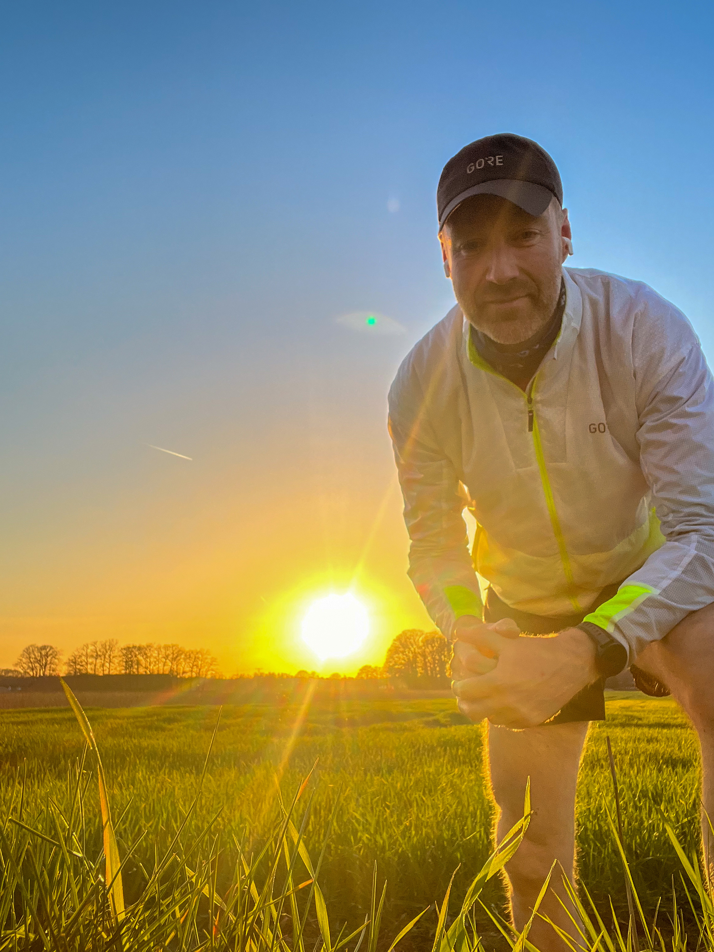 Laechelnder Mann in weisser Jacke und Kappe im goldenen Sonnenuntergangsfeld
